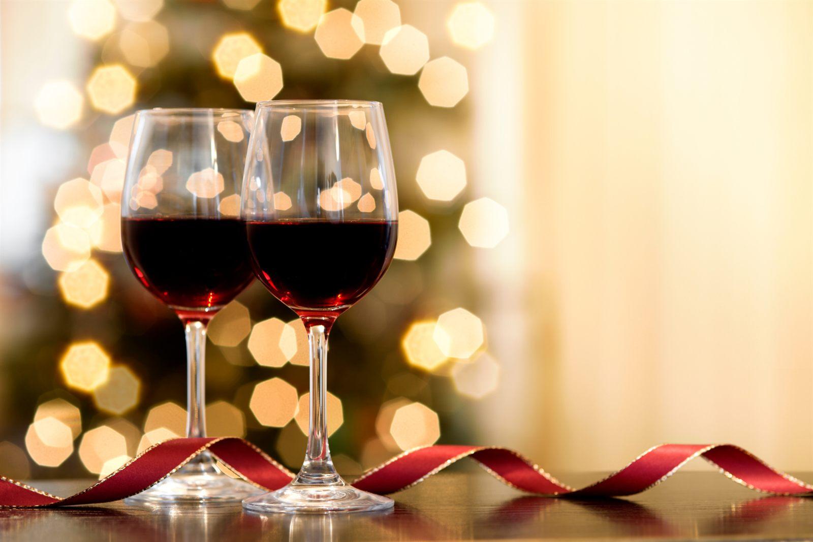 Two glasses of red wine on a table with a red ribbon, holiday lights glowing behind